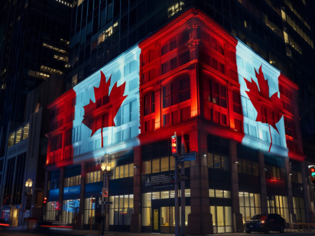An image of a Canadian office building at night, viewed from a corner angle. The building has a big Canadian flag projected on the two sides of the building that are visible from the corner of the intersection.
