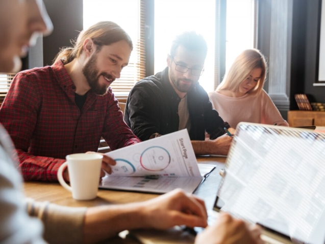 A business meeting with a group of people sitting around a table, reviewing documents.